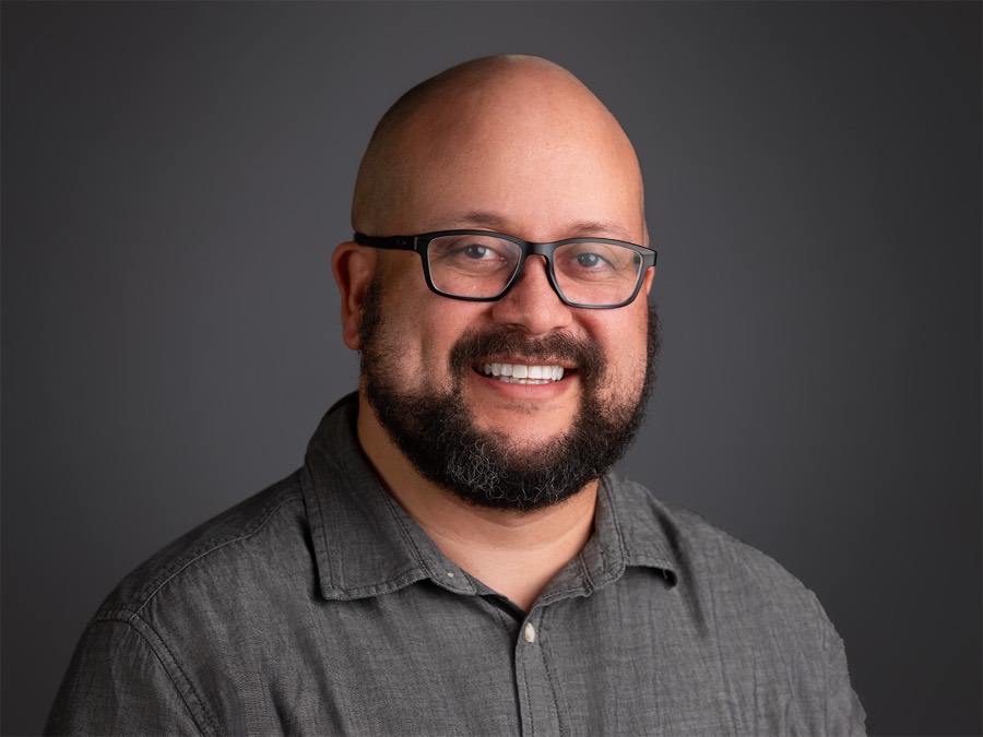 Sam Piñero smiling, wearing glasses and a gray shirt